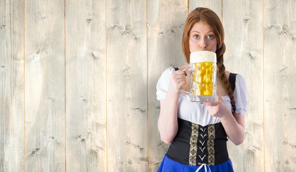 Oktoberfest girl drinking jug of beer against pale wooden planks