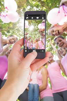 Female hand holding a smartphone against smiling women in pink for breast cancer awareness