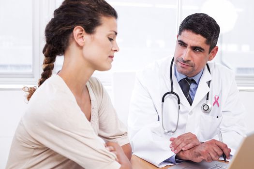 Pink awareness ribbon against doctor and patient in discussion at medical office