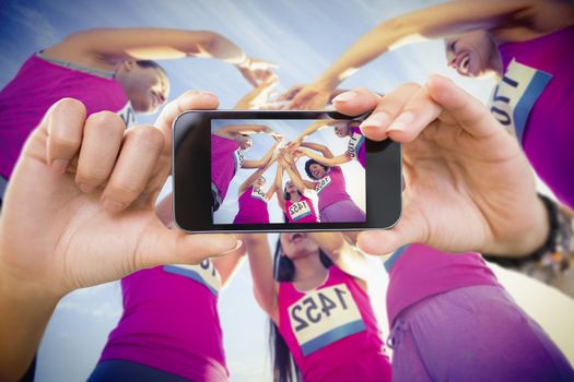 Hand holding smartphone showing against five cheering runners supporting breast cancer marathon