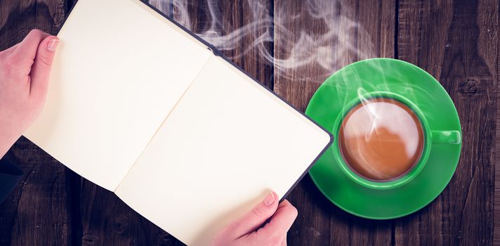 Overhead view of hot tea by hand holding book over wooden table