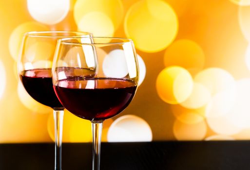 two red wine glasses on wood table against golden bokeh lights background, festive and fun concept