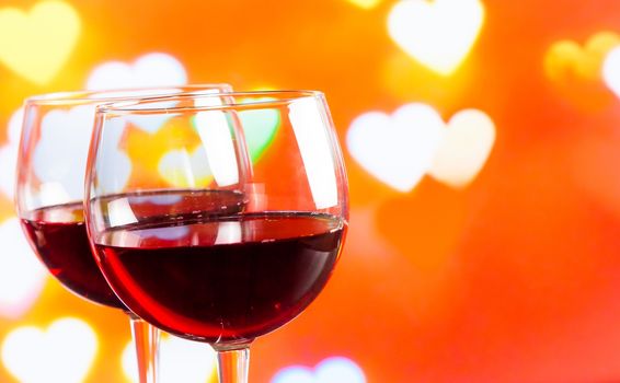 two red wine glasses on hearts decoration bokeh lights background, festive and love concept