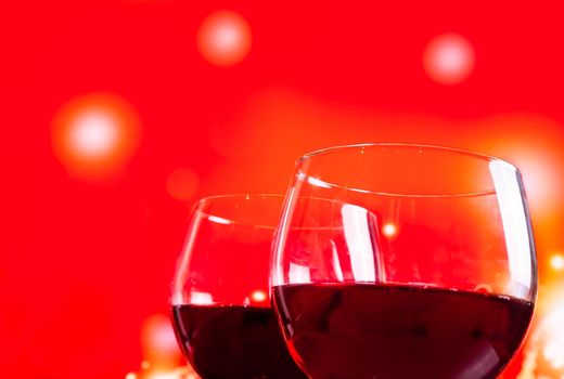 two red wine glasses near the bottle against red lights background, festive and fun concept