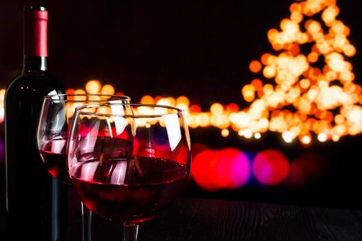 red wine glass near bottle against bokeh lights background, christmas atmosphere