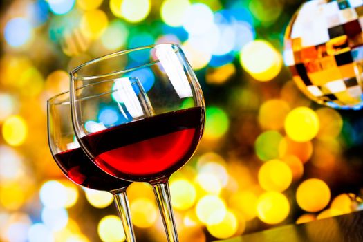 two red wine glasses against colorful bokeh lights and sparkling disco ball background, festive and fun concept