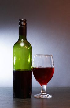 Bottle of red wine near wineglass on nice gray background