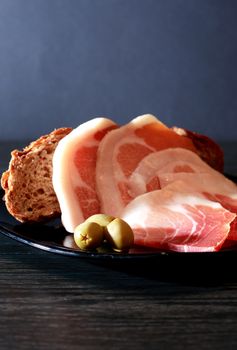 Italian prosciutto. Thin pieces of pork meat near bread and olives