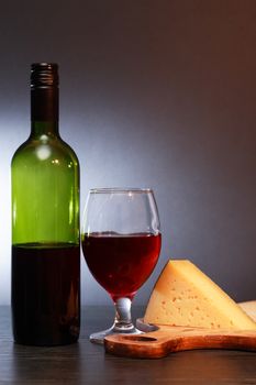 Bottle of red wine near wineglass and piece of cheese on nice gray background