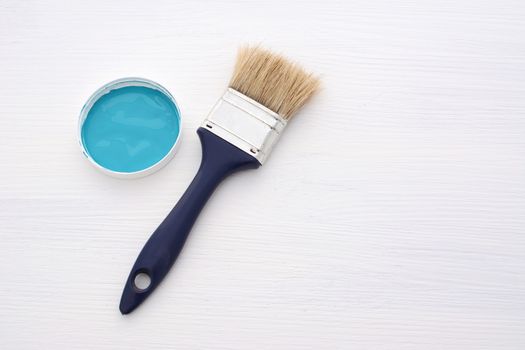 Clean paintbrush and small container of blue paint on a wooden board painted white