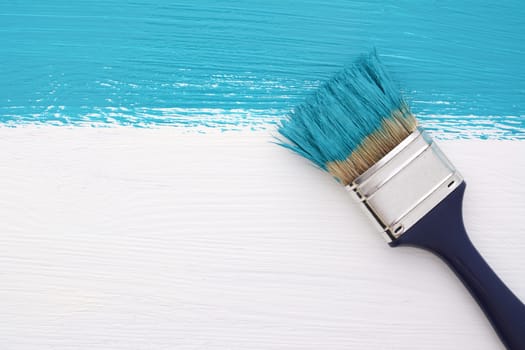 Horizontal stripe of turquoise paint with a dirty paintbrush on a white wooden board