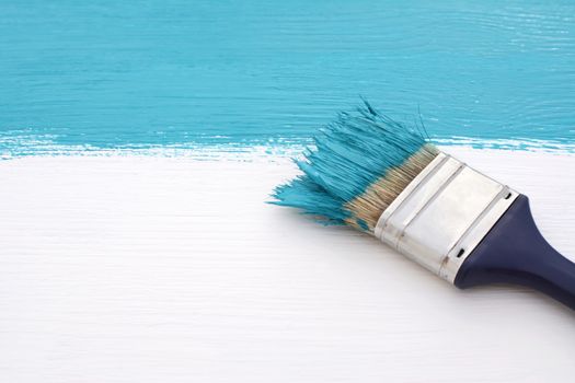 Paintbrush loaded with bold blue paint, painting over white wooden board