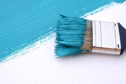 Close-up of paintbrush with paint-covered bristles painting a white board blue