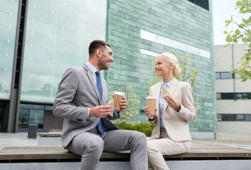 business, partnership, food, drinks and people concept - smiling businessmen with paper cups standing over office building