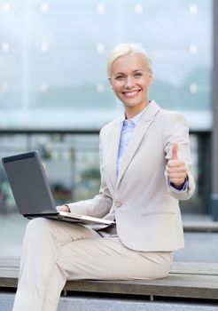 business, education, technology and people concept - smiling businesswoman working with laptop computer on city street