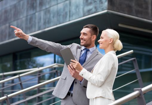 business, partnership, technology and people concept - smiling businessman and businesswoman with tablet pc computer over office building