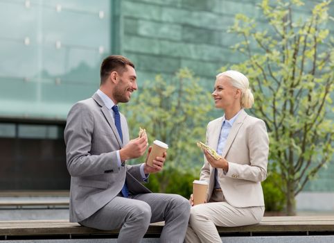 business, partnership, food, drinks and people concept - smiling businessmen with paper cups standing over office building