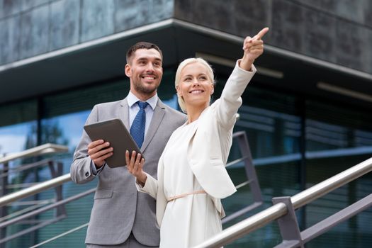 business, partnership, technology and people concept - smiling businessman and businesswoman with tablet pc computer over office building