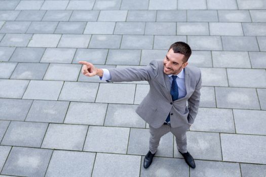 business, development and people and concept - young smiling businessman pointing finger outdoors from top