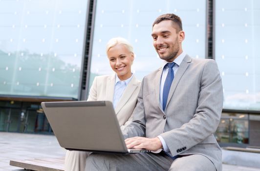 business, education, technology and people concept - smiling businesspeople working with laptop computer on city street