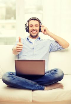 technology, home, music and lifestyle concept - smiling man with laptop and headphones at home showing thumbs up
