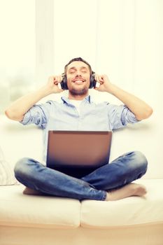 technology, home, music and lifestyle concept - smiling man with laptop and headphones at home