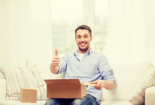 post, home and lifestyle concept - smiling man with cardboard boxes at home showing thumbs up