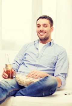 home, technology and entretainment concept - smiling man with beer and popcorn at home