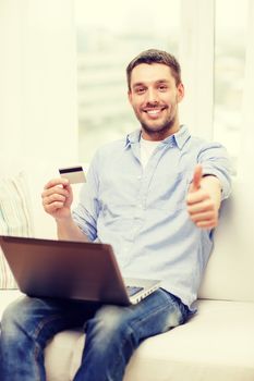 technology, home and lifestyle concept - smiling man working with laptop and credit card at home and showing thumbs up