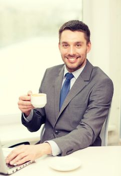 office, business, technology and internet concept - smiling businessman with laptop computer and coffee at office