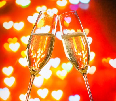 a pair of champagne flutes with golden bubbles make cheers on hearts bokeh background valentine day concept