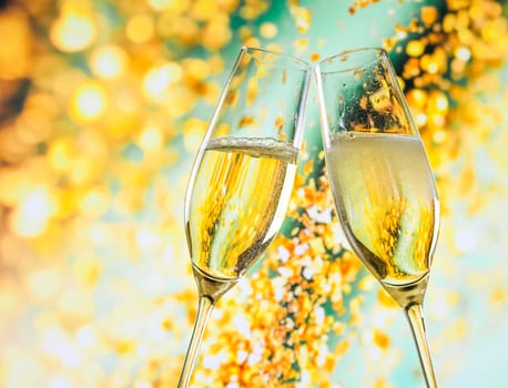 a pair of champagne flutes with golden bubbles make cheers on golden light background with space for text