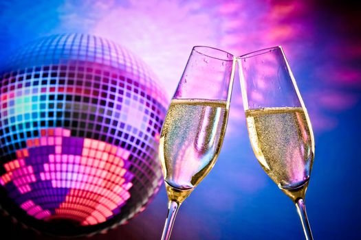 a pair of champagne flutes with golden bubbles make cheers on sparkling blue and violet disco ball background with space for text