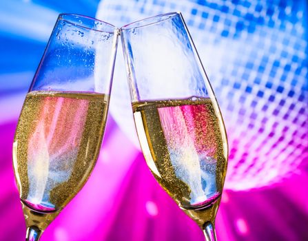 champagne flutes with golden bubbles make cheers on sparkling blue and violet disco ball background with space for text