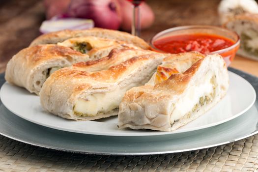 Homemade stromboli or stuffed bread with broccoli potatoes garlic onions and mozzarella cheese along with a side of marinara dipping sauce.