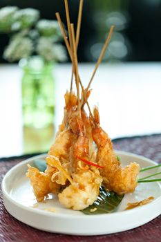 Tempura jumbo shrimp skewers on a white plate standing up vertically.