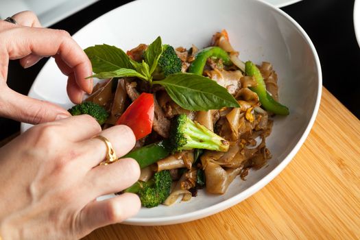 Food stylist grooms a dish by adding sweet basil garnish to the traditional thai dish Pad Kee Mao drunken noodle.