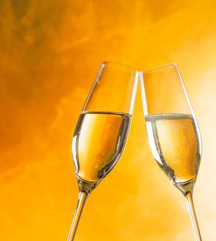 a pair of champagne flutes with golden bubbles make cheers on golden light background with space for text