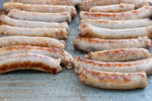 Pictured pork sausages placed in two vertical rows are cooked on the grill.