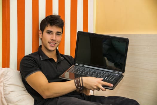 Attractive Young Man with Serious Expression Reclining Comfortably, Showing Laptop on Bed Working on his Start-up Business - Young Male College or University Student Doing Homework, in Bedroom