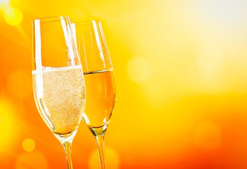 champagne flutes with golden bubbles on golden light background with space for text