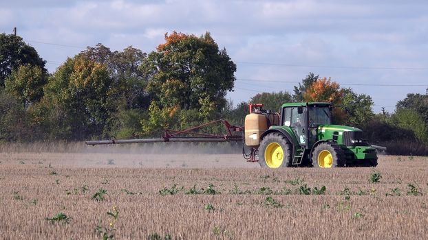 Tractor spraying stubble field with herbicide chemicals in autumn. Farmer with modern vehicle kill weeds in agriculture field before winter.