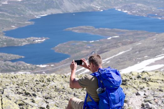 Hiker with big traveling rucksack taking pictures on the phone on the mountain trail, adventure travel and discovery