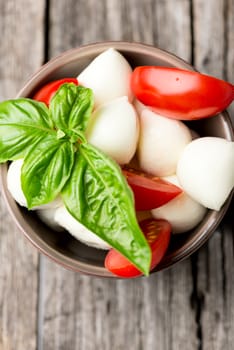 Tomato and mozzarella with basil leaves in bowl on wooden table