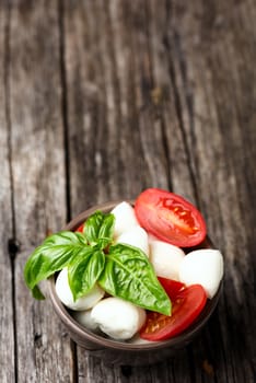 Tomato and mozzarella with basil leaves in bowl on wooden table