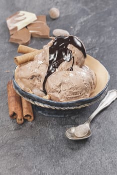 Chocolate ice cream scoops with chocolate topping, nuts and cinnamon on dark granite table. Macro photograph with shallow depth of field.