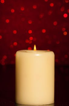 candle with flame on wood table and red bokeh background and space for text