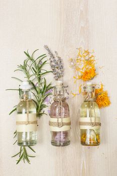 Row of essential oils in glass bottles, rosemary, lavender and calendula, on the wooden board.