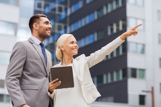 business, partnership, technology and people concept - smiling businessman and businesswoman with tablet pc computer over office building