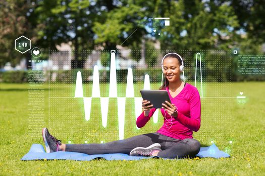 fitness, park, technology and sport concept - smiling african american woman with tablet pc computer and headphones on mat outdoors